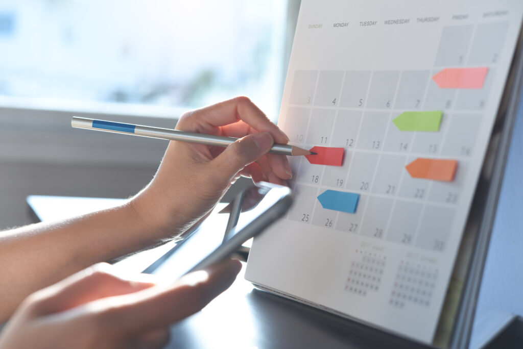 Frau plant Termine mit Kalender und Smartphone am Schreibtisch