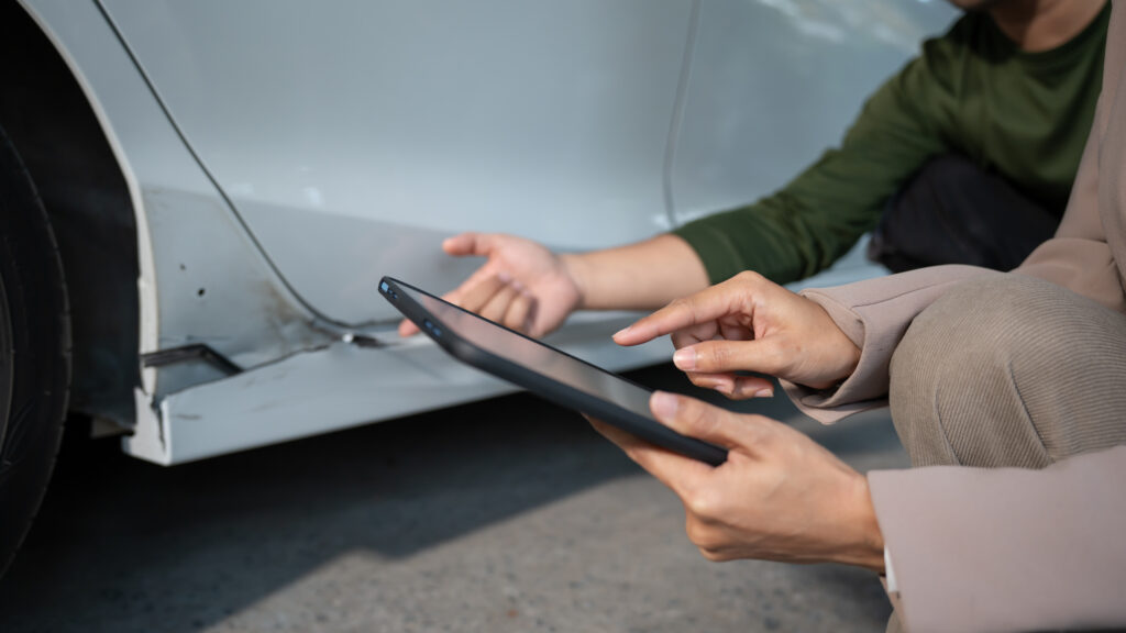 Personen begutachten Karosserieschaden am Auto mit einem Tablet